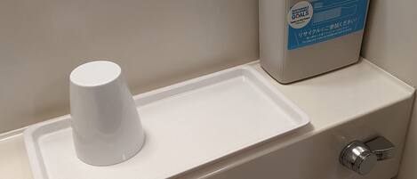 Des toilettes comprenant un urinoir blanc, une poubelle et un distributeur de savon.