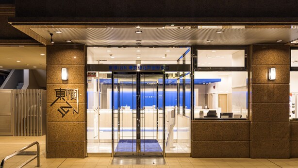 Entrada de hotel con puerta giratoria, recepción y un letrero con caracteres japoneses.
