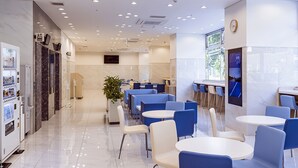 Un comedor moderno con sillas azules y blancas, una máquina expendedora y una planta grande en maceta.
