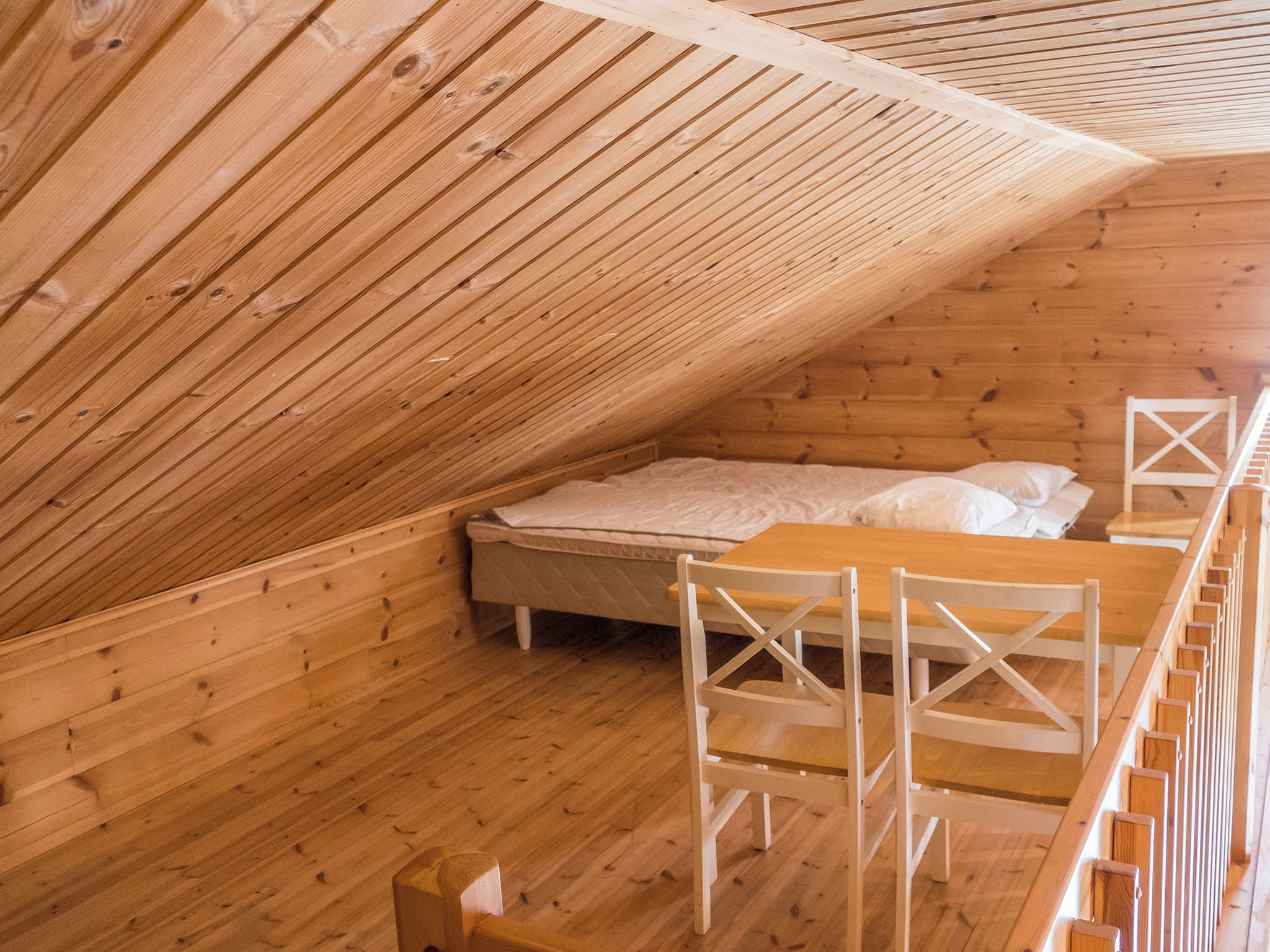 Una cabaña de madera con techo inclinado, una cama con ropa de cama blanca y una mesa de madera con sillas.