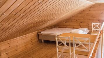 A wooden cabin with a sloped ceiling, a bed with white bedding, and a wooden table with chairs.