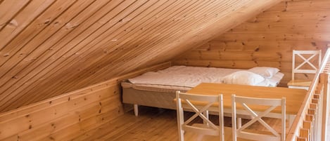 A wooden cabin with a sloped ceiling, a bed with white bedding, and a wooden table with chairs.