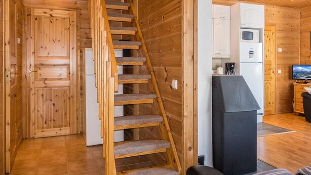 Ein Holzinnenraum mit einer Treppe zu einem Schlafzimmer im oberen Bereich, einem Küchenbereich mit Geräten und einem Fernseher.