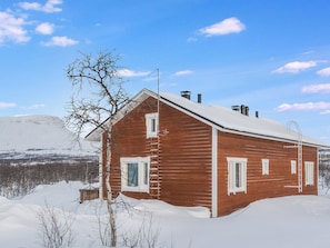 A wooden cabin with a snow-covered roof, surrounded by a snowy landscape and a clear sky. - Saana 1 by Interhome (Enontekiö)