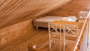 Eine Holzhütte mit geneigtem Dach, einem Bett, einem Tisch und Stühlen.