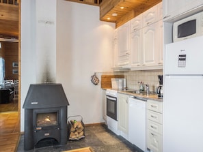 A kitchen with white cabinets, a built-in oven, a microwave, and a wood-burning stove.