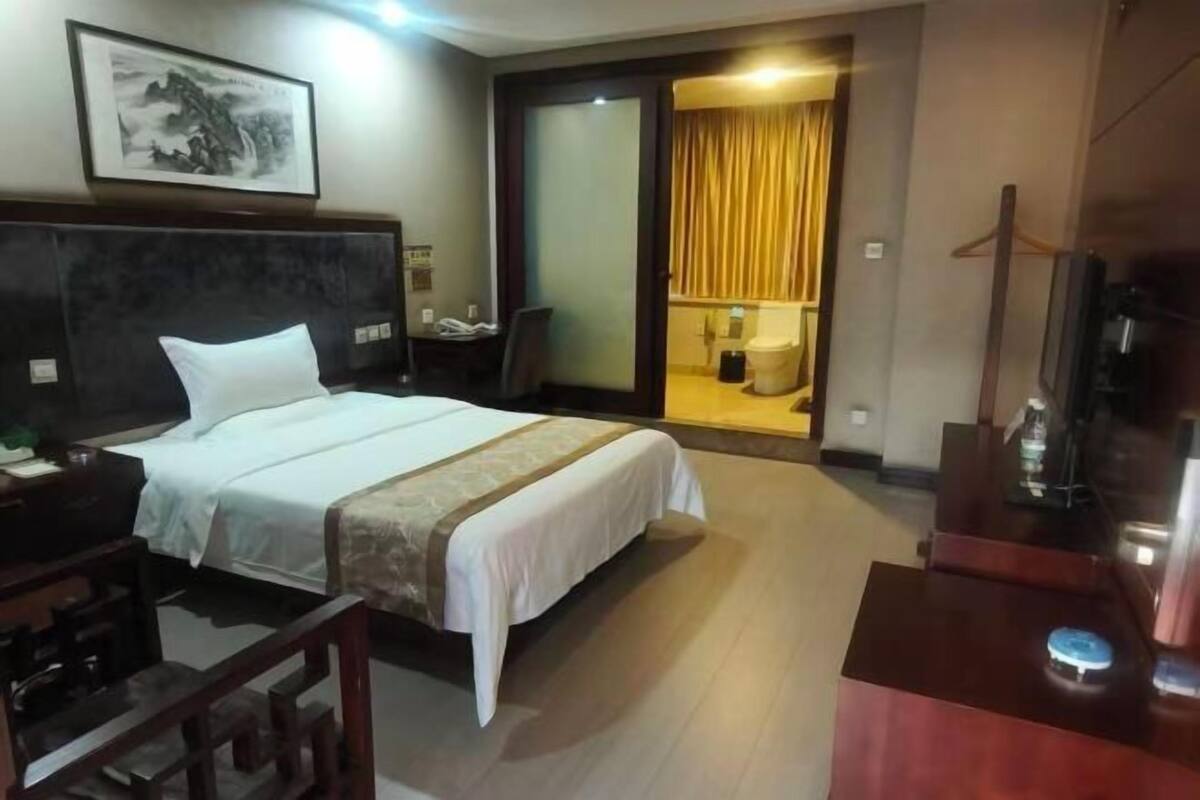 A hotel room with a large bed, a desk with a computer, a television, and a bathroom visible through an open door.