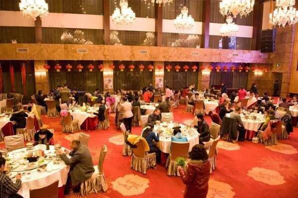 Een feestzaal met ronde tafels, kroonluchters en rode lantaarns.