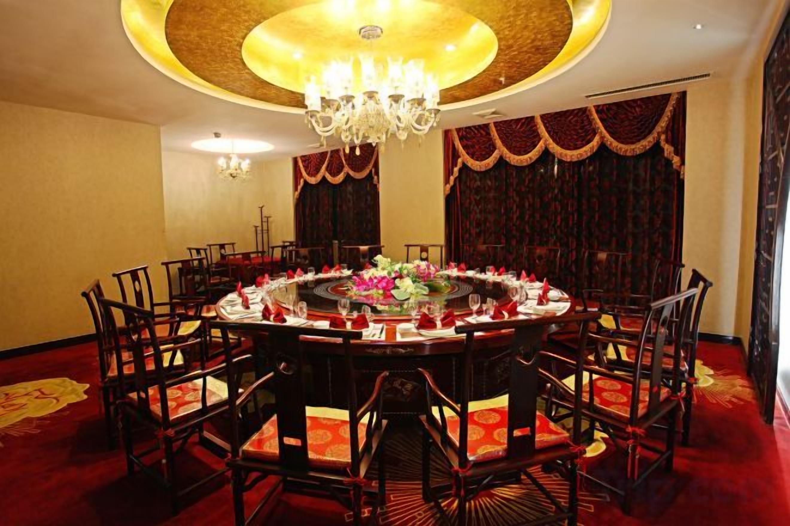 Une table de salle à manger ronde, avec des chaises, un lustre et des rideaux rouges.