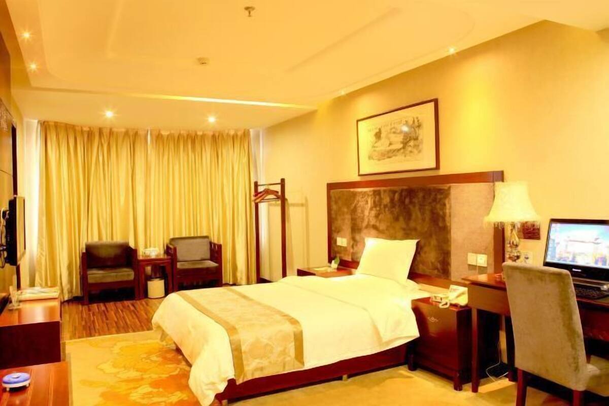 A hotel room with a large bed, a desk with a computer, a chair, and a television.