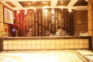 A reception area with a wall of calligraphy, a reception desk, and a tiled floor. - Laoying International Hotel (Danjiangkou)
