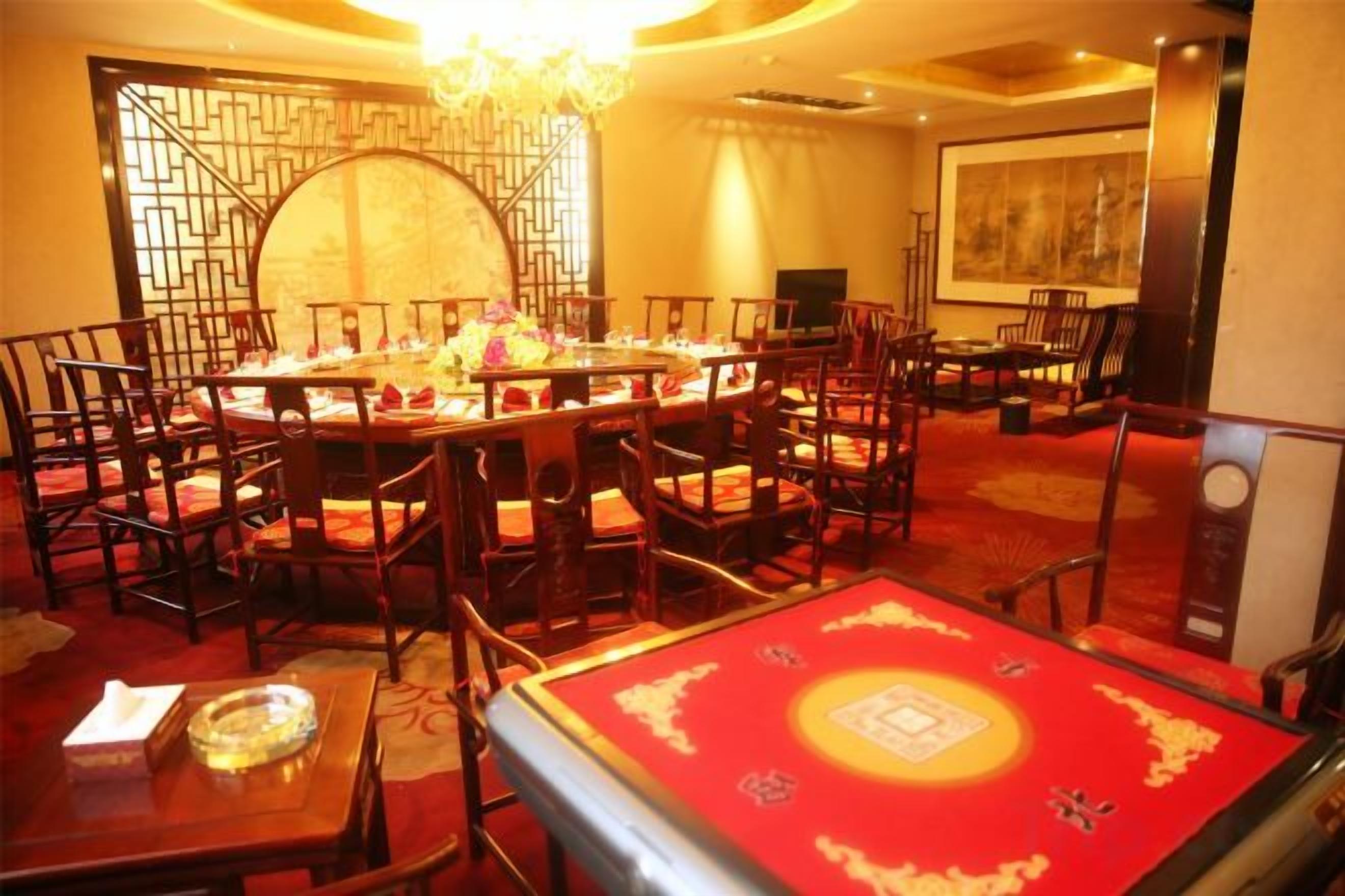 A traditional dining area with round tables and chairs, a chandelier, and a red carpet.