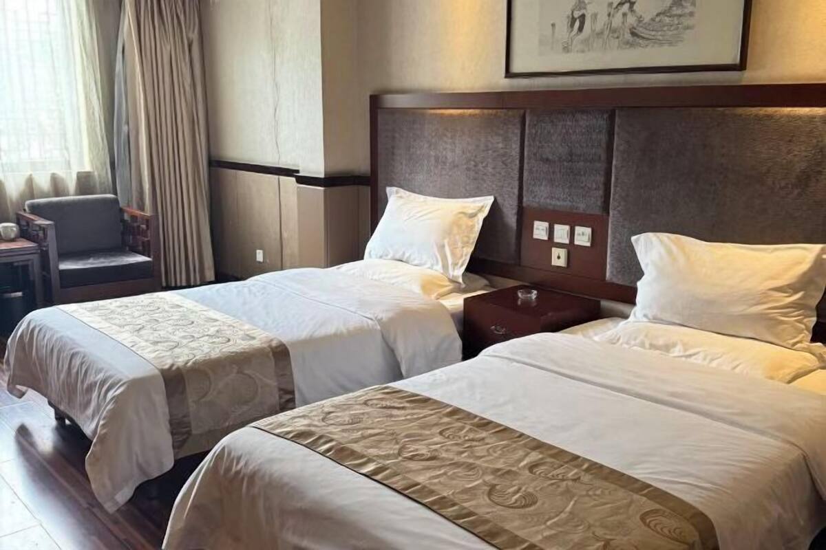 A hotel room with two beds, a chair, a nightstand, and a painting on the wall.