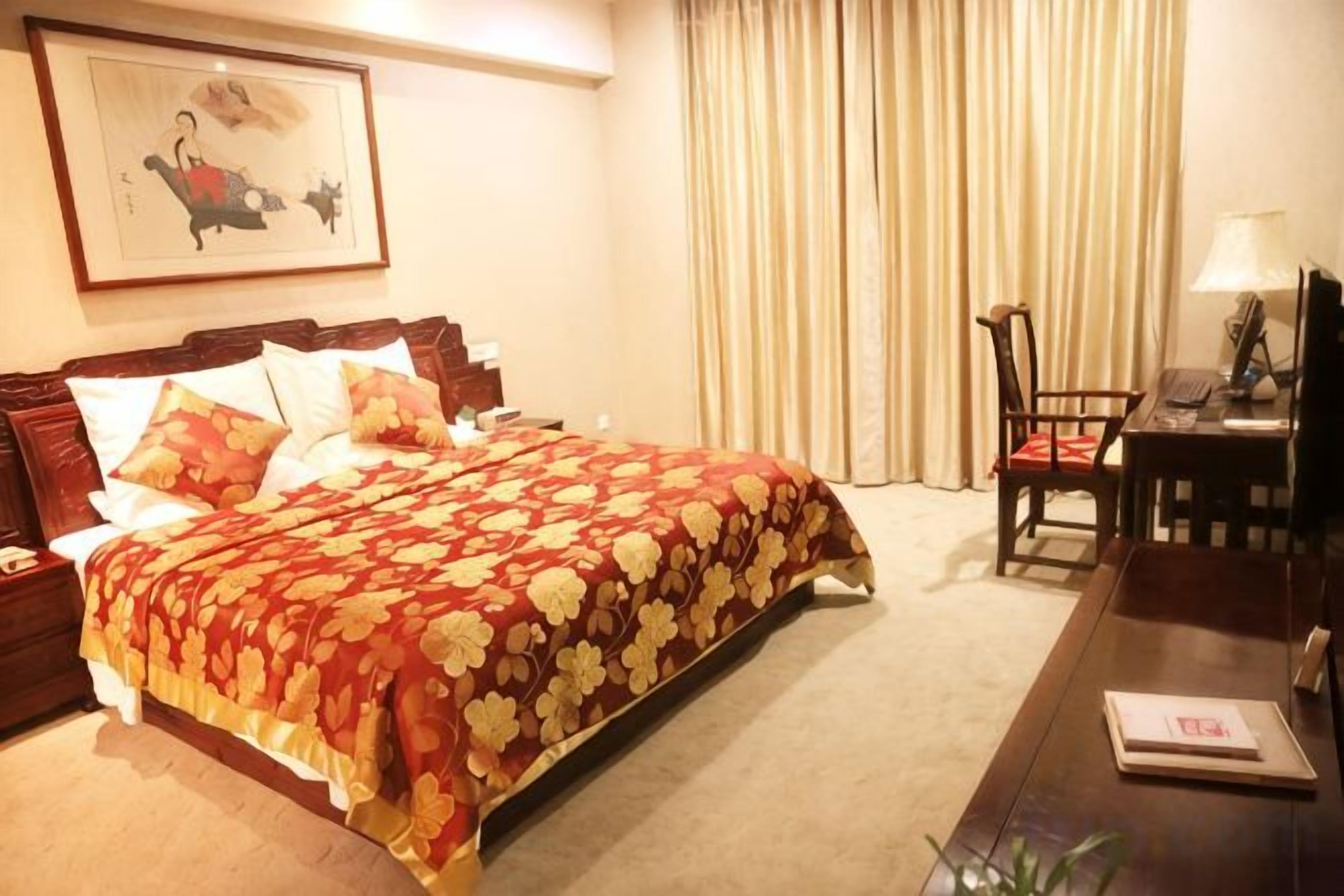 A hotel room with a bed, a desk, a chair, a lamp, and a painting on the wall.
