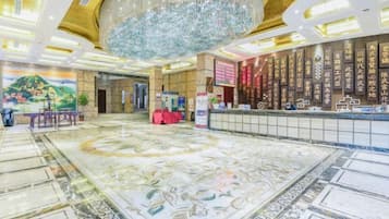 A hotel lobby with a large chandelier, a reception desk, and a decorative floor.