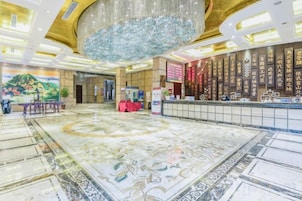 A hotel lobby with a large chandelier, a reception desk, and a decorative floor.