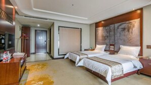 Hotellihuone, jossa on kaksi sänkyä, työpöytä ja suuri taideteos seinällä.