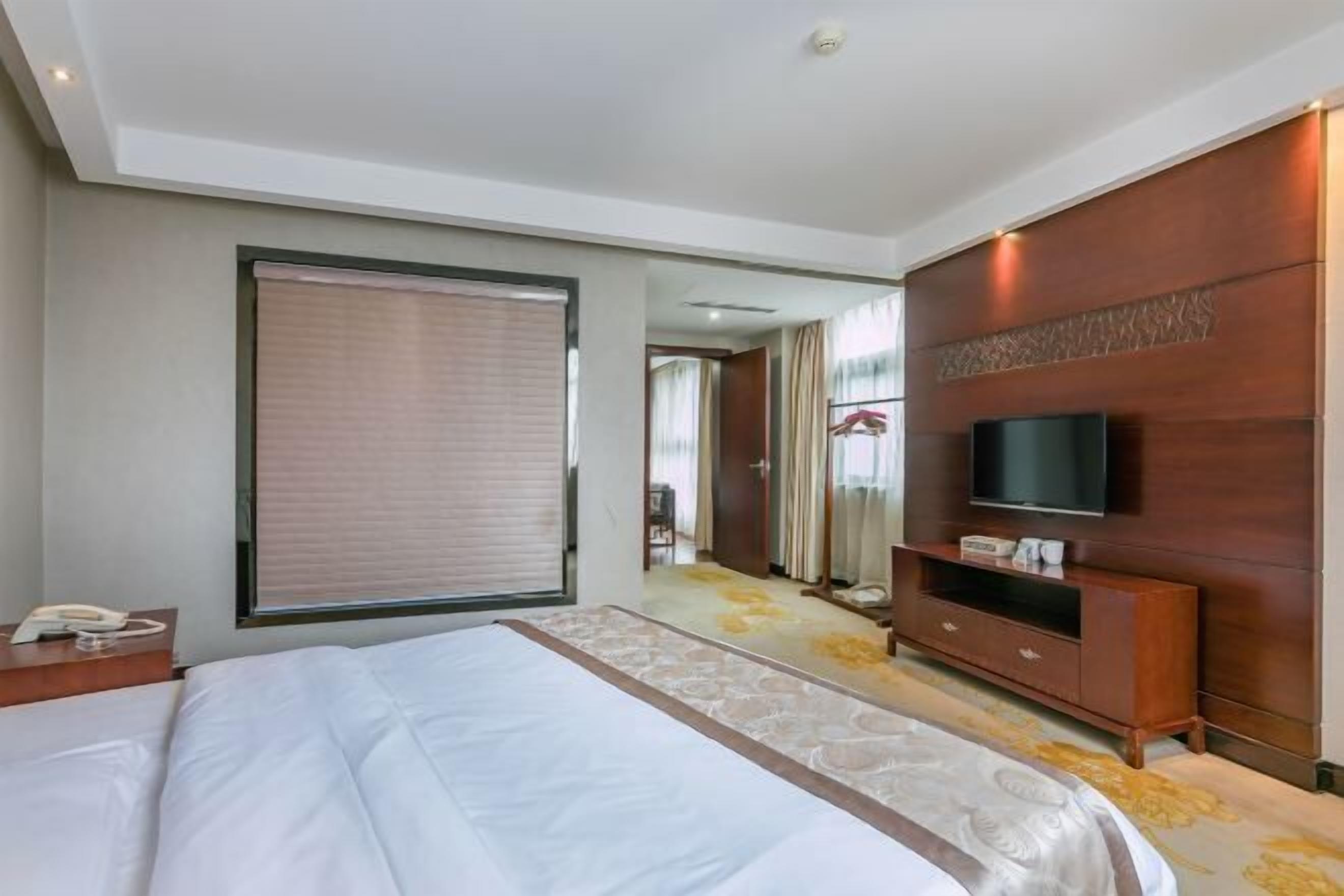 A hotel room with a large bed, a TV on a wooden cabinet, and a bathroom visible through an open door.