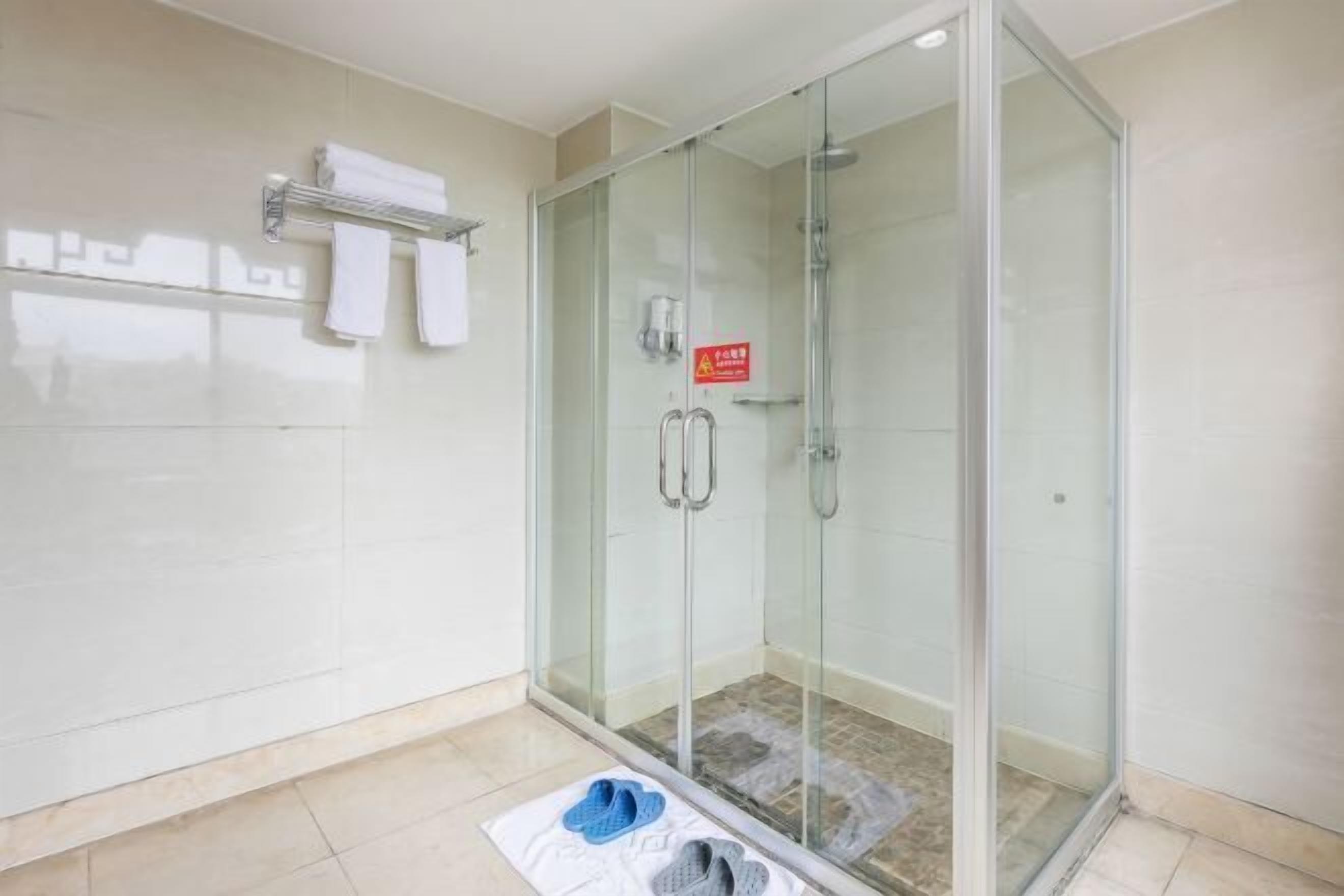 Een moderne badkamer met een douche met glazen wand, een handdoekhouder en een paar slippers op de vloer.