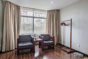Una habitación con piso de madera, dos sillas, una mesita, un perchero y una ventana con cortinas.