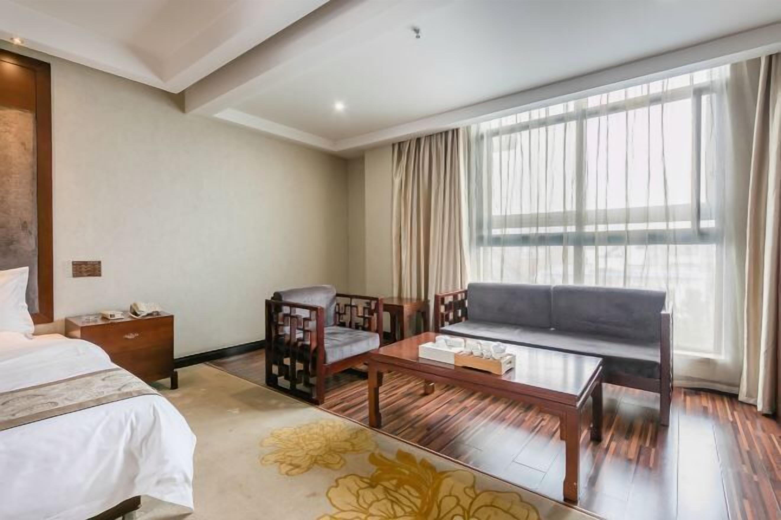 A hotel room with a bed, a sofa, a chair, a small table, and a window with curtains.