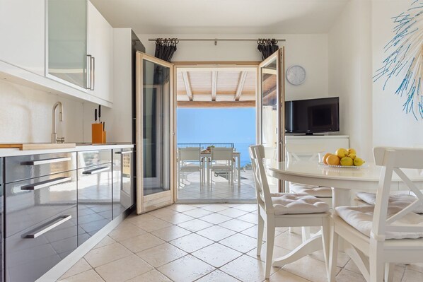 Une cuisine moderne avec vue sur la mer, un coin repas avec des meubles blancs et un téléviseur fixé au mur.