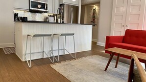 Ett modernt kök med en köksö i mitten, barstolar, en röd soffa och ett träbord.