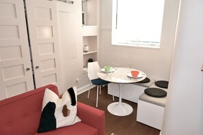 Un espacio habitable compacto con un sofá rojo, una mesa de comedor blanca con sillas y una pequeña kitchenette.