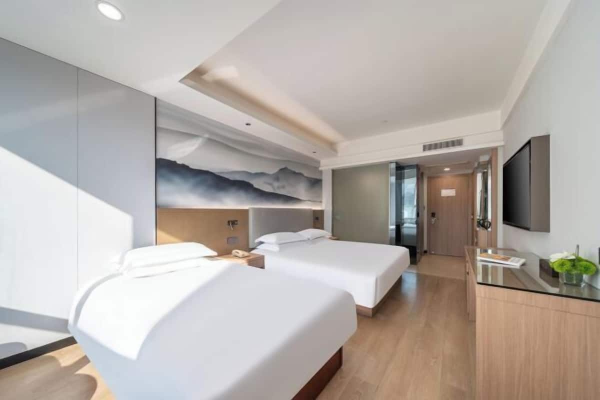 A modern hotel room with two beds, a desk, a flat-screen TV, and a mural on the wall.