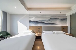 A hotel room with two beds, a green chair, a painting of mountains, and a wooden floor.