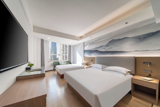 A modern hotel room with two beds, a large TV, a desk with a chair, and a city view.