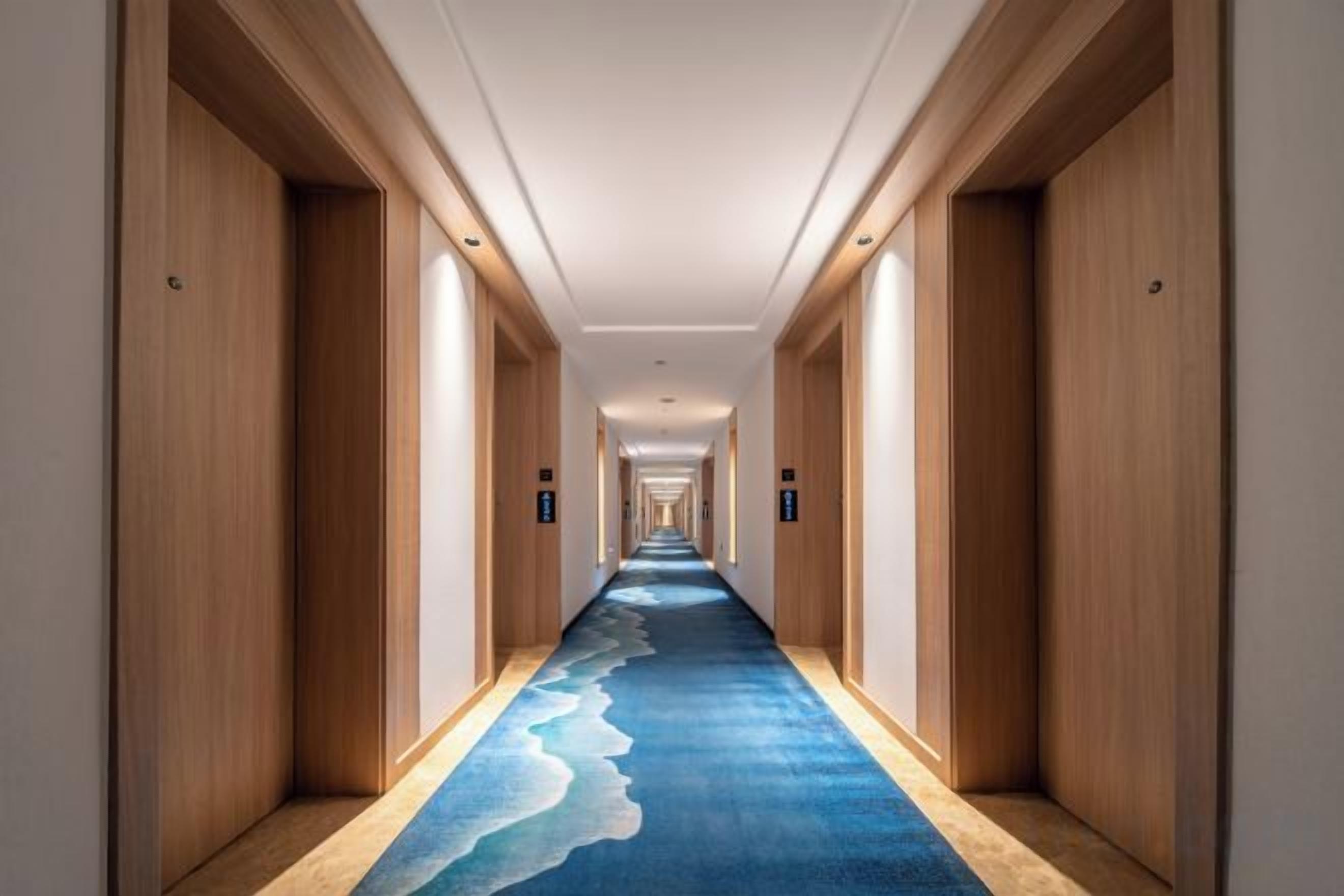 A hotel hallway with a carpet featuring a wave design, wooden walls, and doors on both sides.