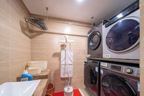 A laundry room with stacked washing machines, a drying rack, and a sink.
