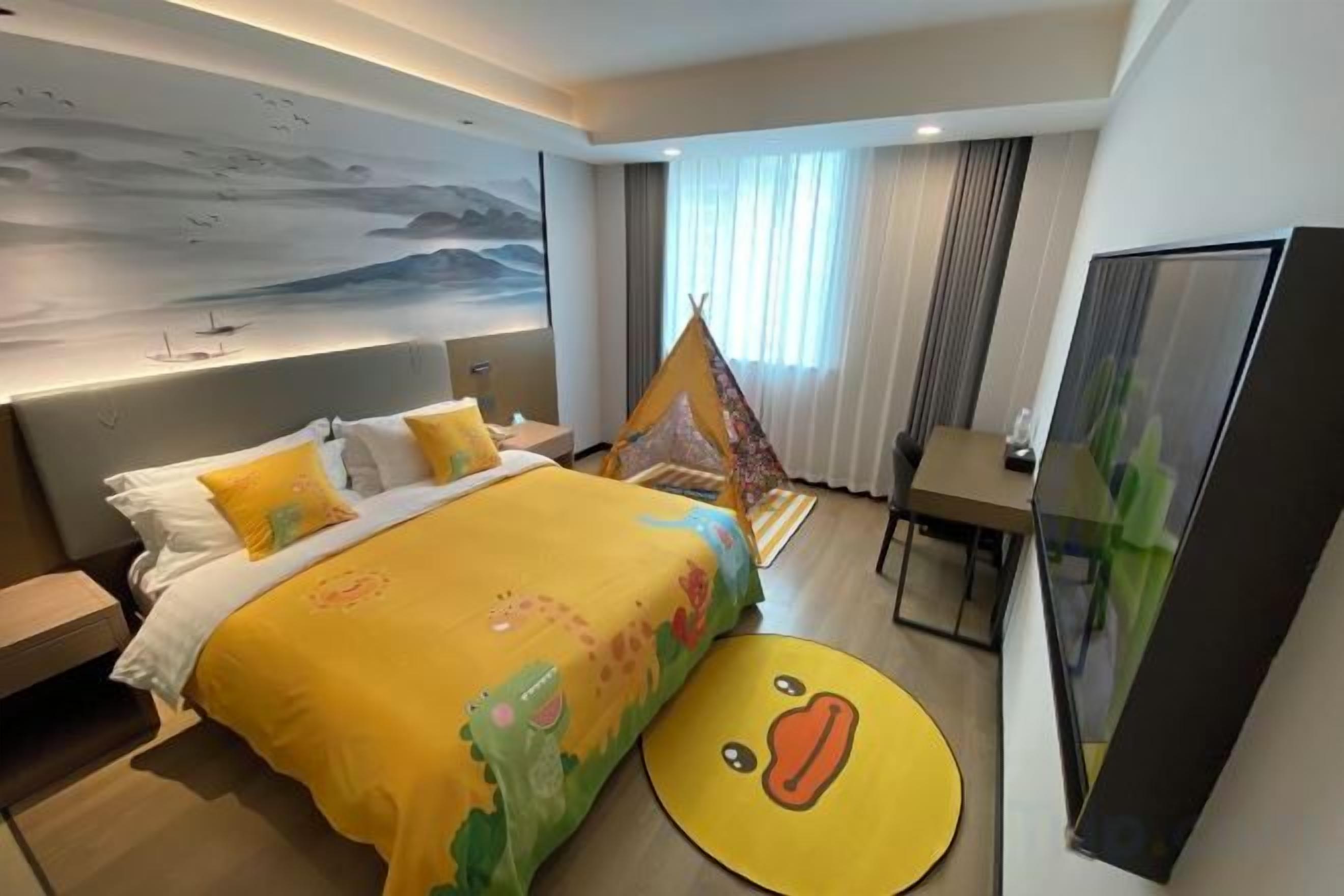 A hotel room with a bed, a desk, a chair, a window with curtains, and a painting on the wall.