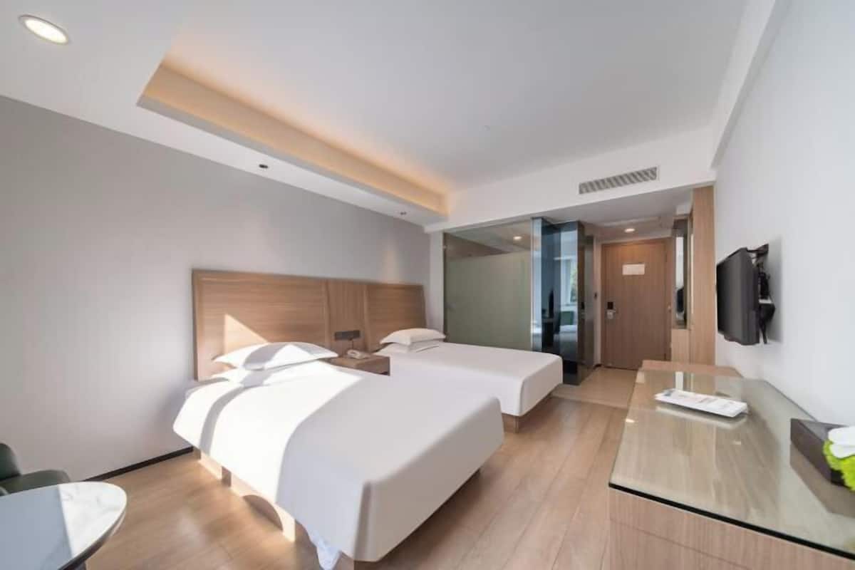 A modern hotel room with two beds, a desk, a TV, and a glass partition.