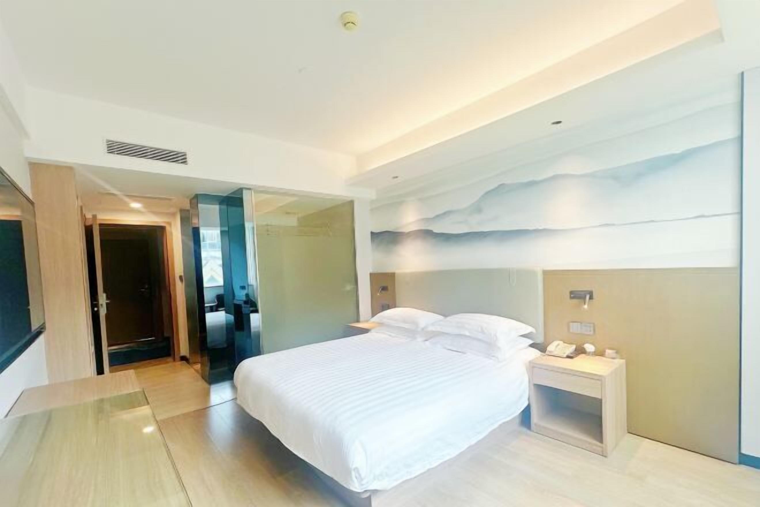 Une chambre d’hôtel moderne avec un grand lit, une table de chevet avec une lampe et un téléphone fixé au mur.