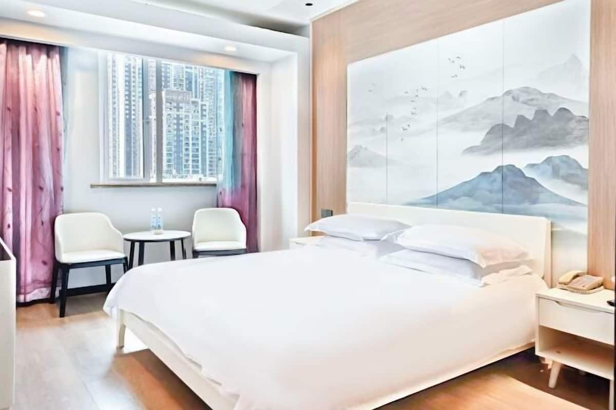 A hotel room with a bed, a desk, a chair, a window with curtains, and a large painting on the wall.