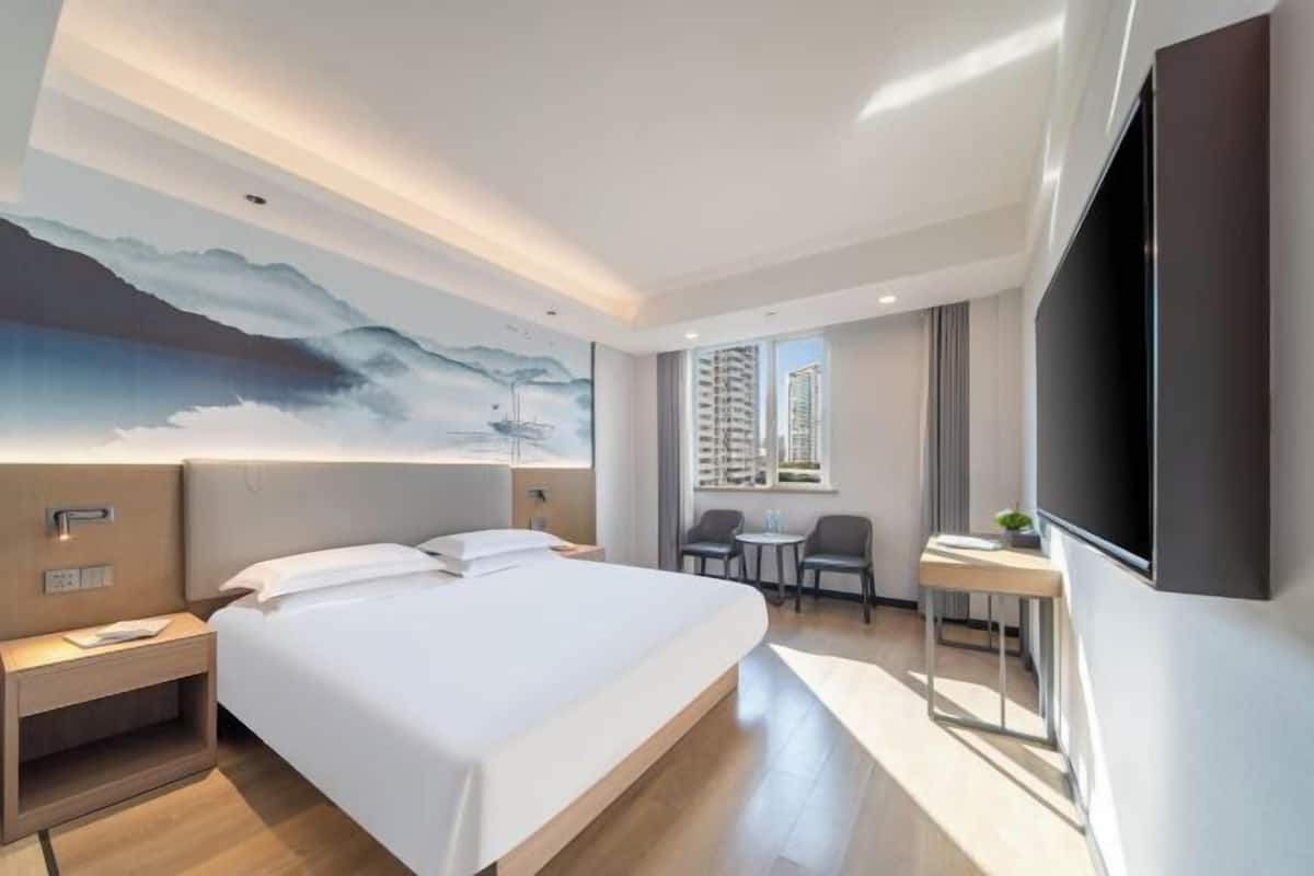 A modern hotel room with a large bed, a desk, a chair, a TV, and a mural on the wall.