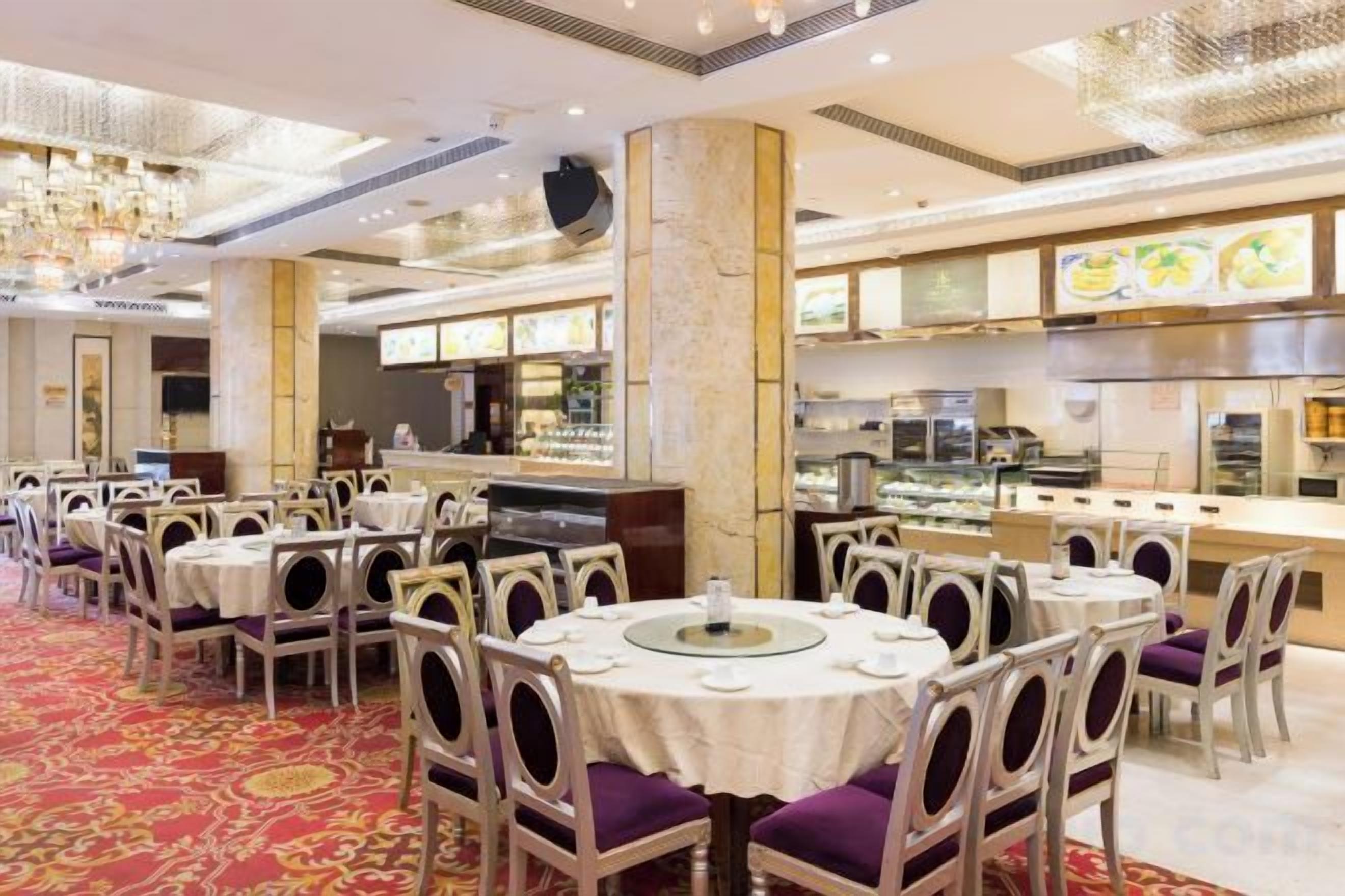 A restaurant with round tables, chairs, a bar area, and a kitchen in the background.