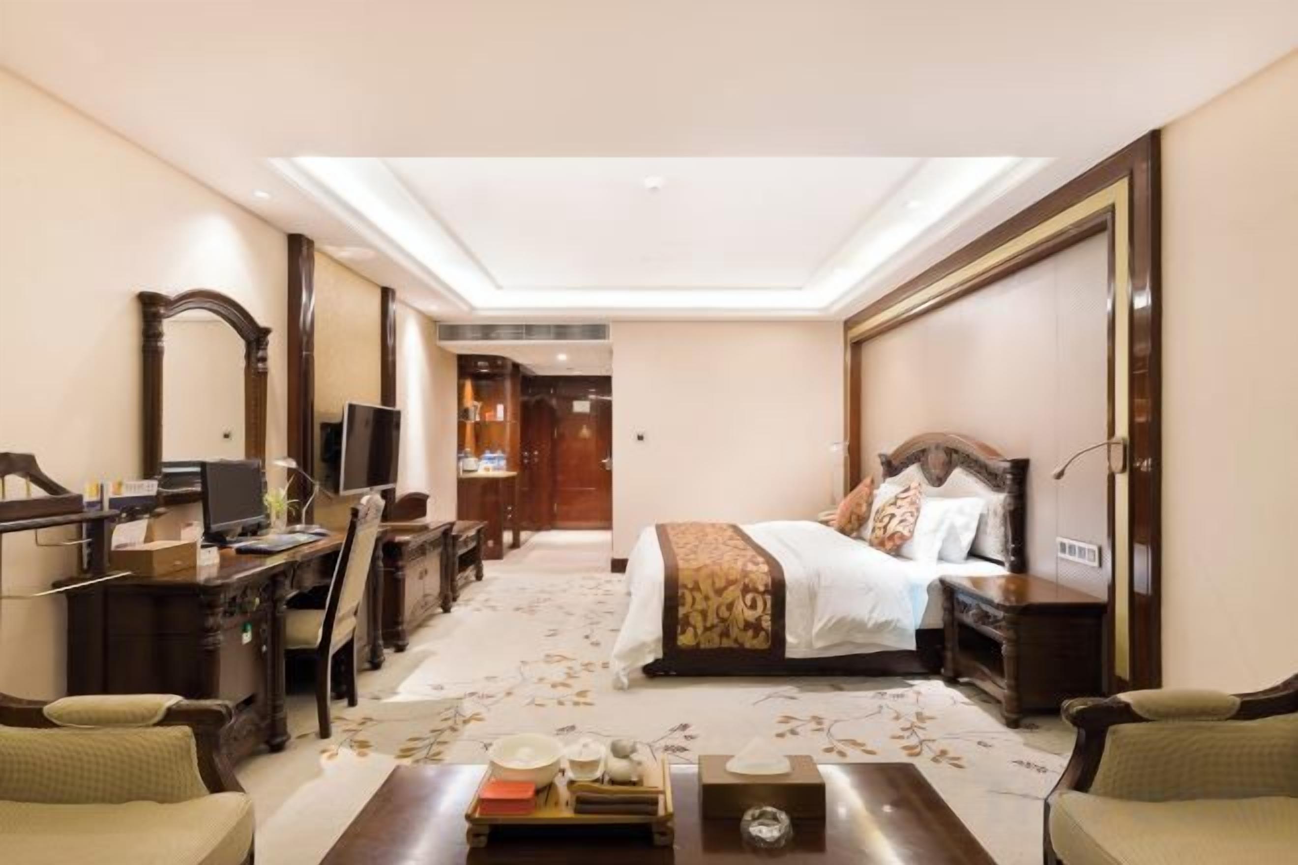 A hotel room with a bed, desk, chair, and a television.