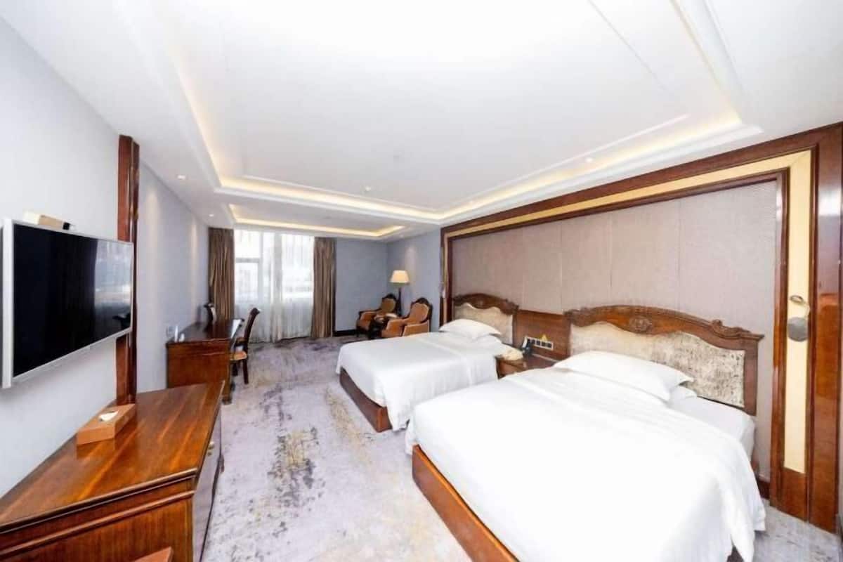 A hotel room with two beds, a TV, a desk, and a chair.