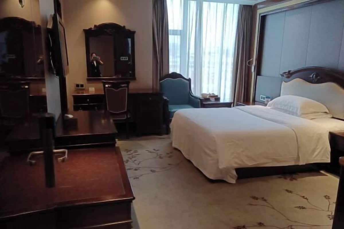 A hotel room with a bed, a desk, a chair, a dresser, and a mirror.