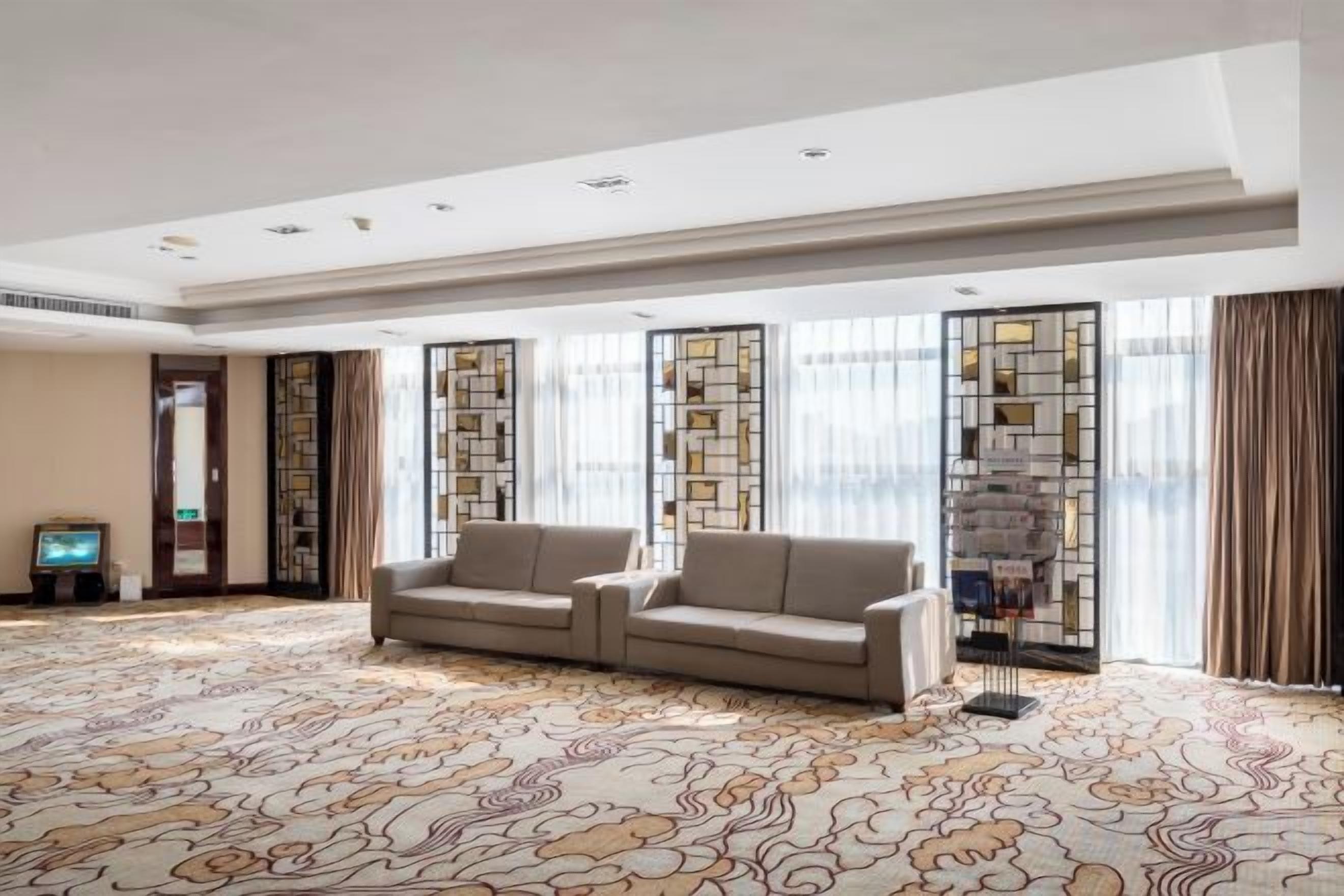 A spacious hotel room with a large sofa, a flat-screen TV, and a patterned carpet.