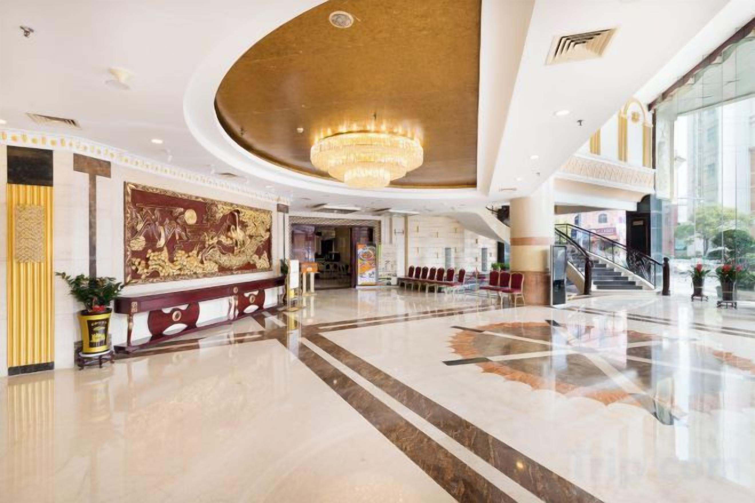 A spacious lobby with a grand chandelier, a reception desk, and a staircase leading to upper floors.