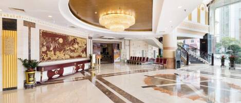 A spacious lobby with a grand chandelier, a reception desk, and a staircase leading to upper floors.