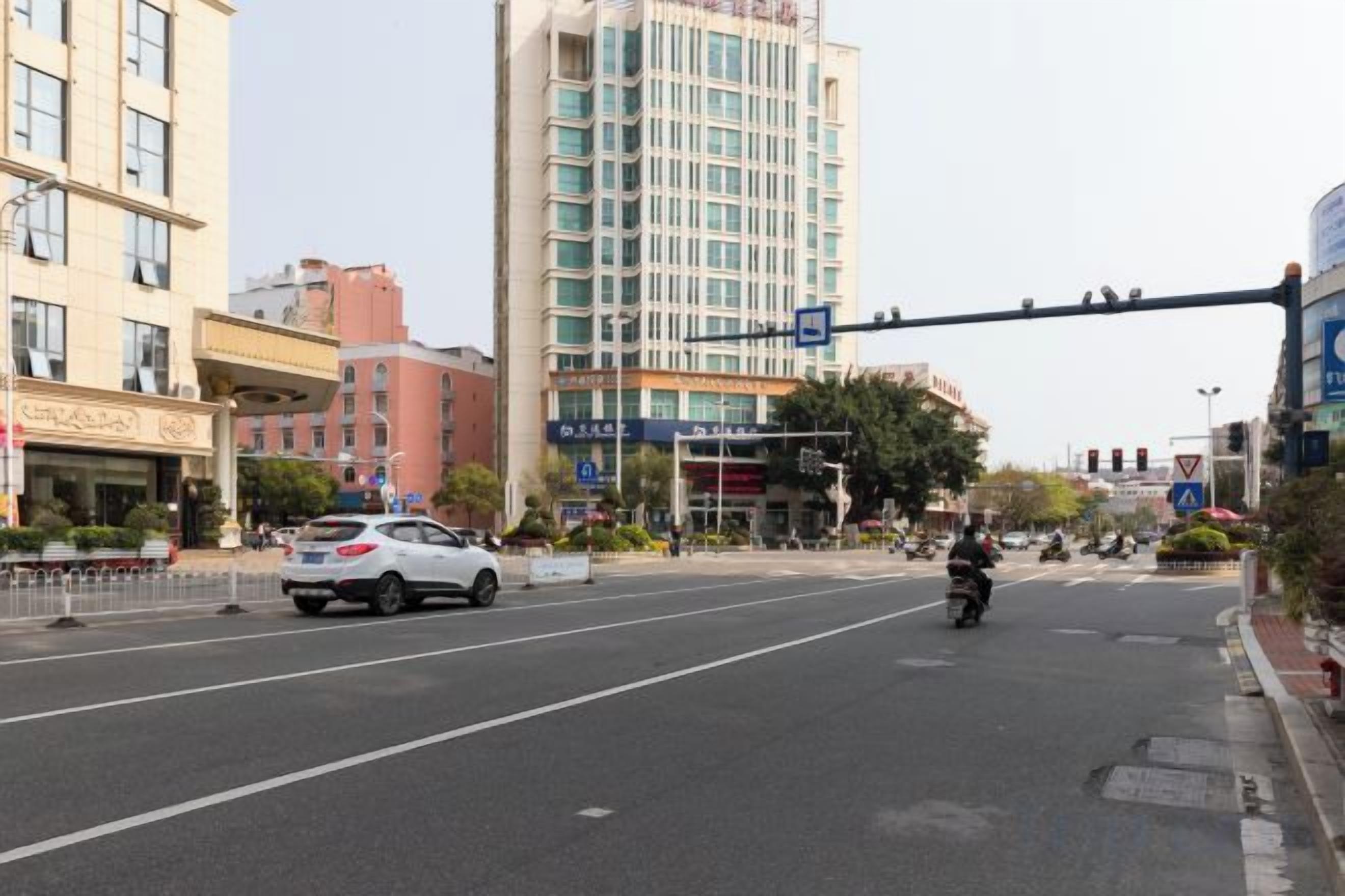 Une vue de rue avec une voiture blanche, une moto et un passage pour piétons.