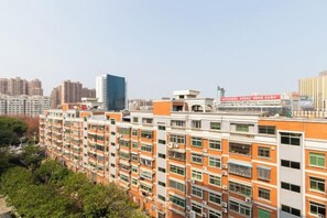 Un edificio residencial de varios pisos con balcones, cielo despejado y un rascacielos distante.