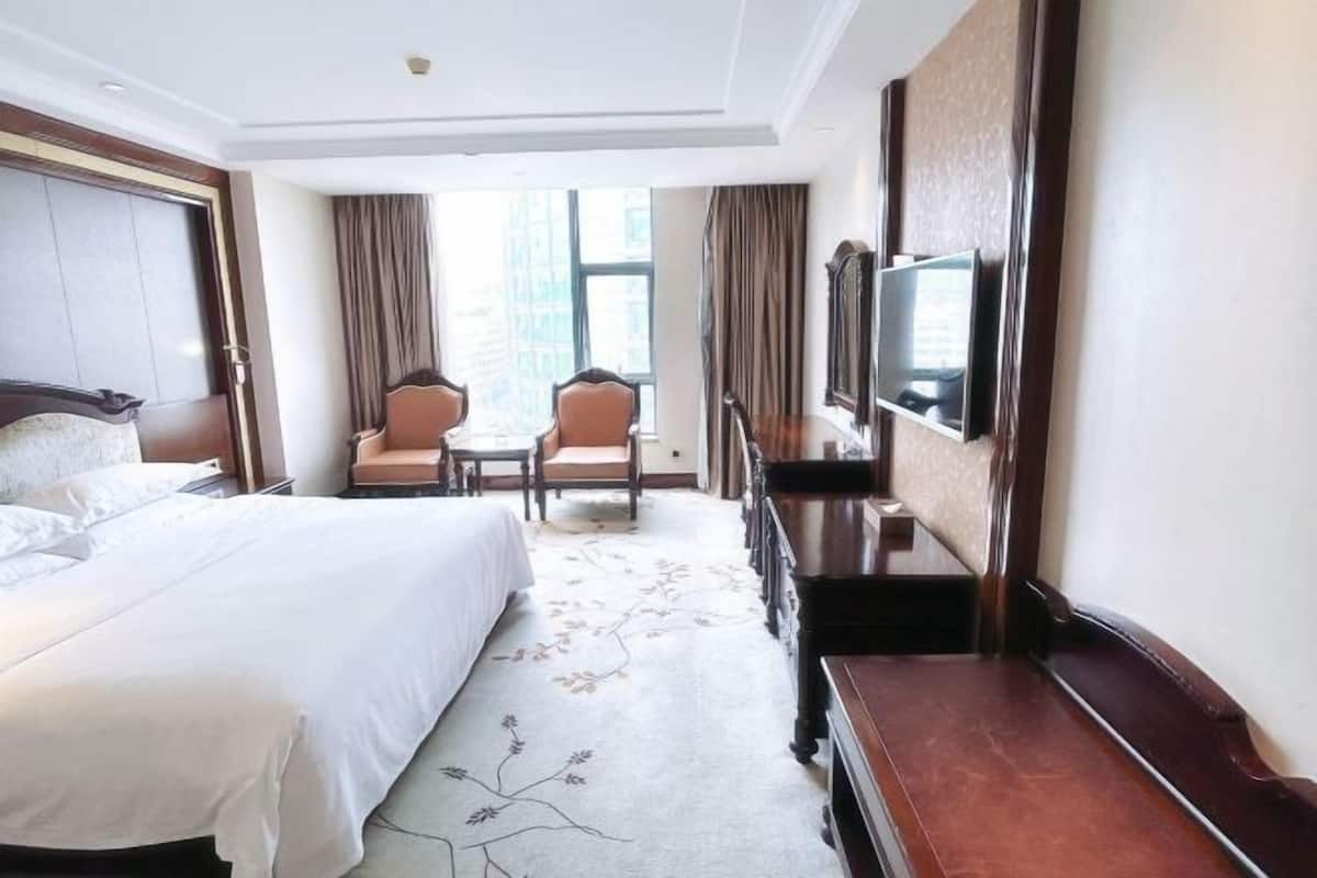 A hotel room with a large bed, a desk, a chair, a TV, and a window with curtains.