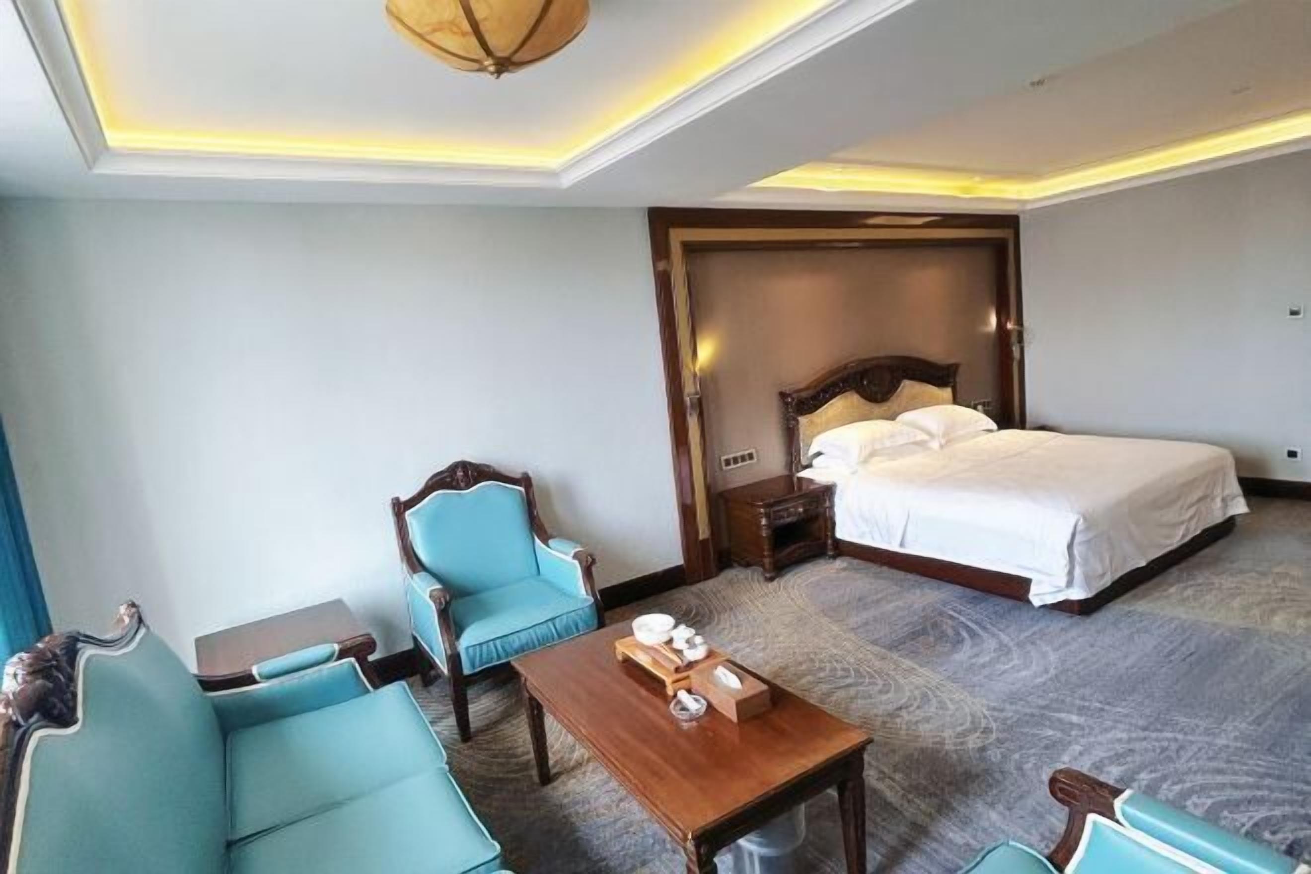Habitación de hotel con una cama, dos sillones, una mesita y una lámpara en el techo.