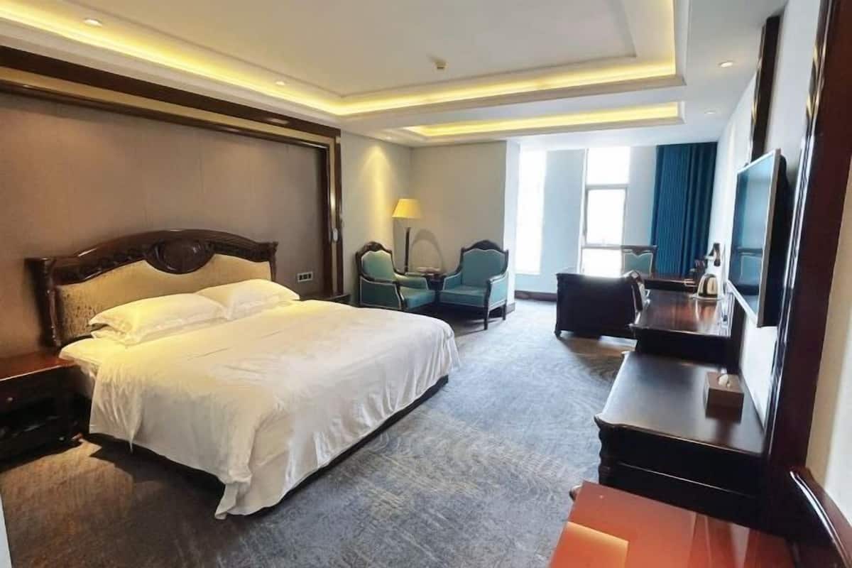 A hotel room with a large bed, a desk with a TV, a chair, and a lamp.